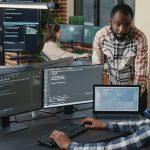 Programer sitting at desk with multiple screens running code talking with colleague about artificial intelligence algorithm. Software developers doing innovative artificial intelligence project. SSUCv3H4sIAAAAAAAAA01Su44bMQz8F9UmImn1dJkAqVOkO6SgJMoWbr0y9pHDwfC/h+vzJVElckbikMObaEUchcKcgsMMEnUBE7SDWEOBAaVLmZIM0YiDKLiSOKpBx8FLbZS3Ru7nIBIuLYvjTbRx3JZ1xrX1SRwZmWkqND+uVNra54YjR/eDWFZct4UWfsZR5r9PjD7iz/9ebnueBf6kfJ762E/vLGPZEqe+9ct1W2lexP3wSfu6LW2iZfnyvU04ZfpL/kH9OtJ/zL+IuP86CDzRlN93Ifdd8Uj40PUidAhBDwVB14xglFUQtCqAwZisUx58zPtgVHWZUbBWaTBFJ0BDEWTxpiqVqiuSaSrFKGvh4TpbwXjDtEEjIGVTBixe1X3MHiUlLStQsQFM1ZHroYZISieszgUVmBbiUK3JDhIWw9qq5aKqglbaR5+S88YzjXzVWRcFeojcgqUKmB23EGNRSROGkpiGqgYprYSqnGdaMiyrElQKhbyMPIC9BW+z1AN3ik5KMJkMhDpkUNH7GLMMVttHp54/YzC7zDQVEBI5CcmhRU2GpPWCB//6xg5enivQ1/O+KWxR36Z1fv+waez9ionNO1YcFzqIMy4LE8ozwQ+vc8ttOj0XifevXz7uU193Hx9urz2/tvIs9bF758bZvc5NbNexY6HyhLd0aev6Gc70u9HbP/b9fv8DTRVWOjkDAAA=